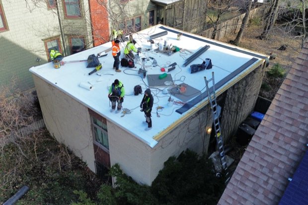 Crew working a small commercial roof, bare winter canopy around the building.