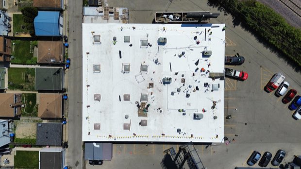 Aerial over a completed reflective roof, residential blocks behind.