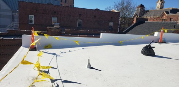 Membrane field with layout markers and a masonry parapet beyond.