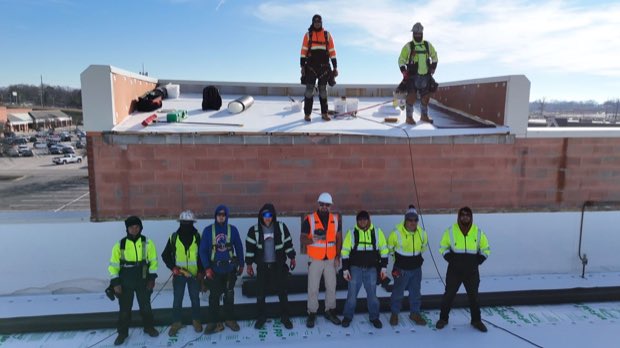 Crew on a completed roof section, block parapet and flat coastal terrain beyond.