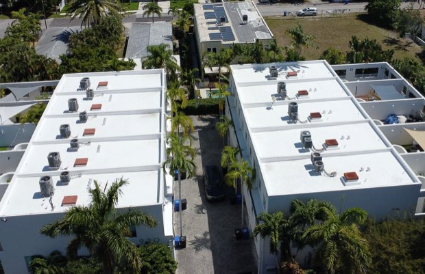 Two completed reflective roofs with rooftop mechanical units, palms between the buildings.