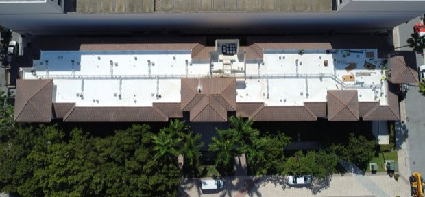 Long residential building with tile and reflective sections, palms along the frontage.