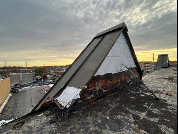 Storm-damaged roof at dusk — membrane and decking lifted clear of the structure.